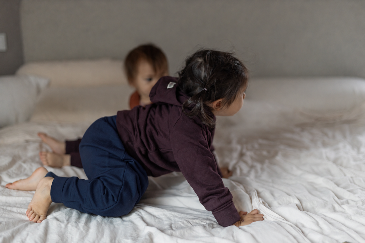 Krabbelndes Kleinkind auf einem Bett in einer Hose aus Every Day Merino mit umgeschlagenen Bündchen